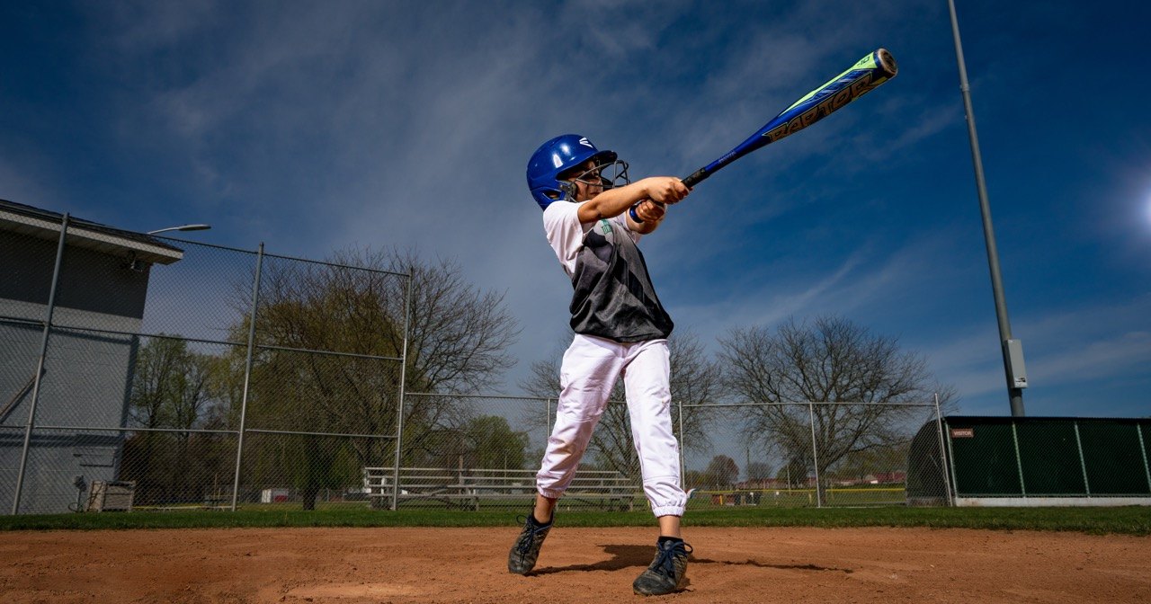 Young baseball player in a blue helmet finishing his swing at home plate under a big blue sky