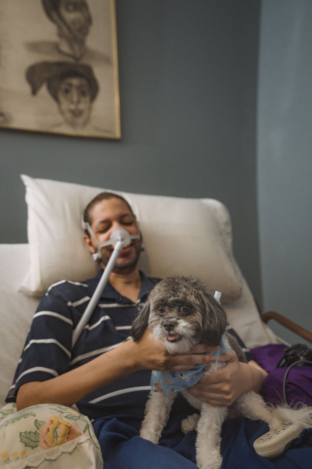 A patient at home with a ventilator mask, holding a small dog
