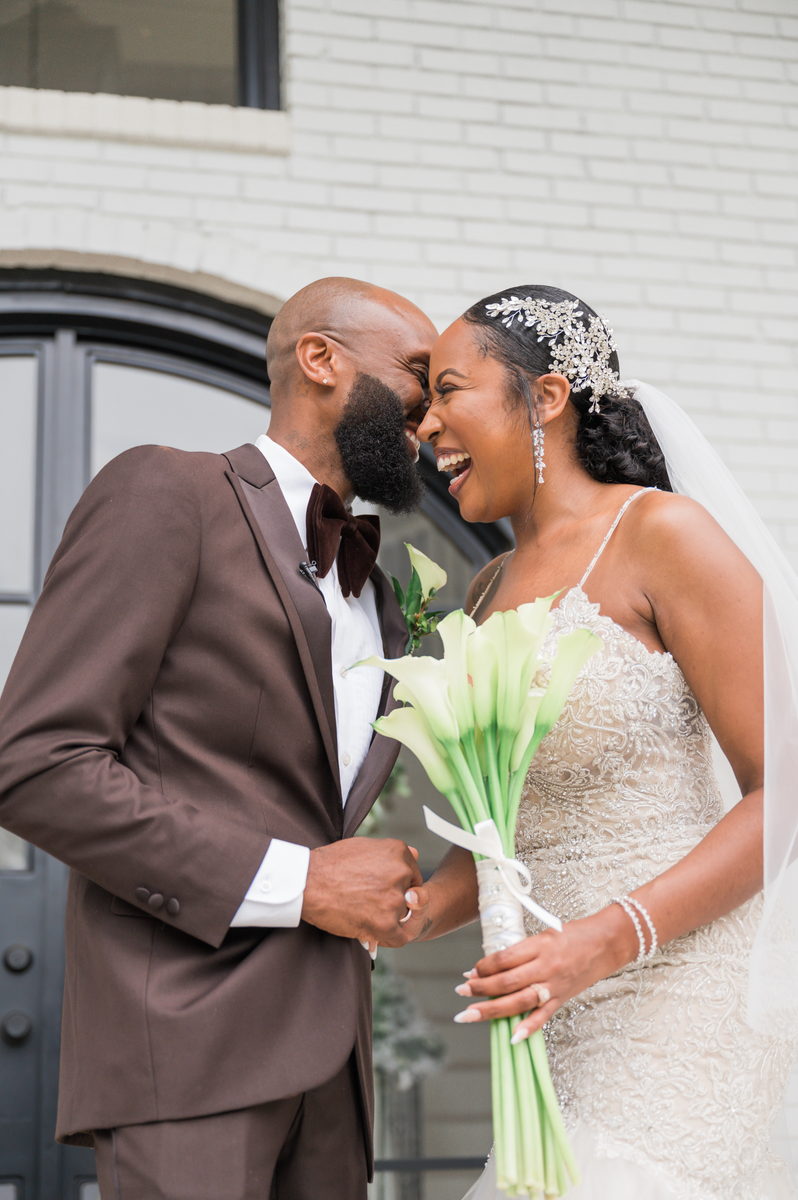 Anjanette and Ritchie laughing with calla lilies at a black arched door