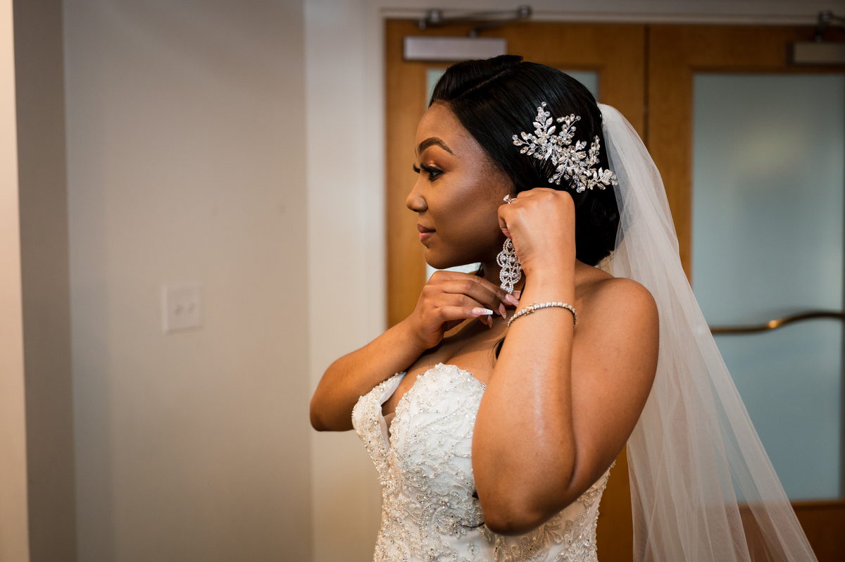 Haley fastening an earring, veil in soft window light