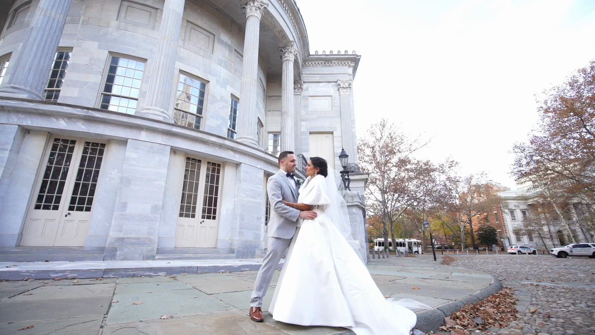 Alyssa and Will embracing on the plaza before the marble columns