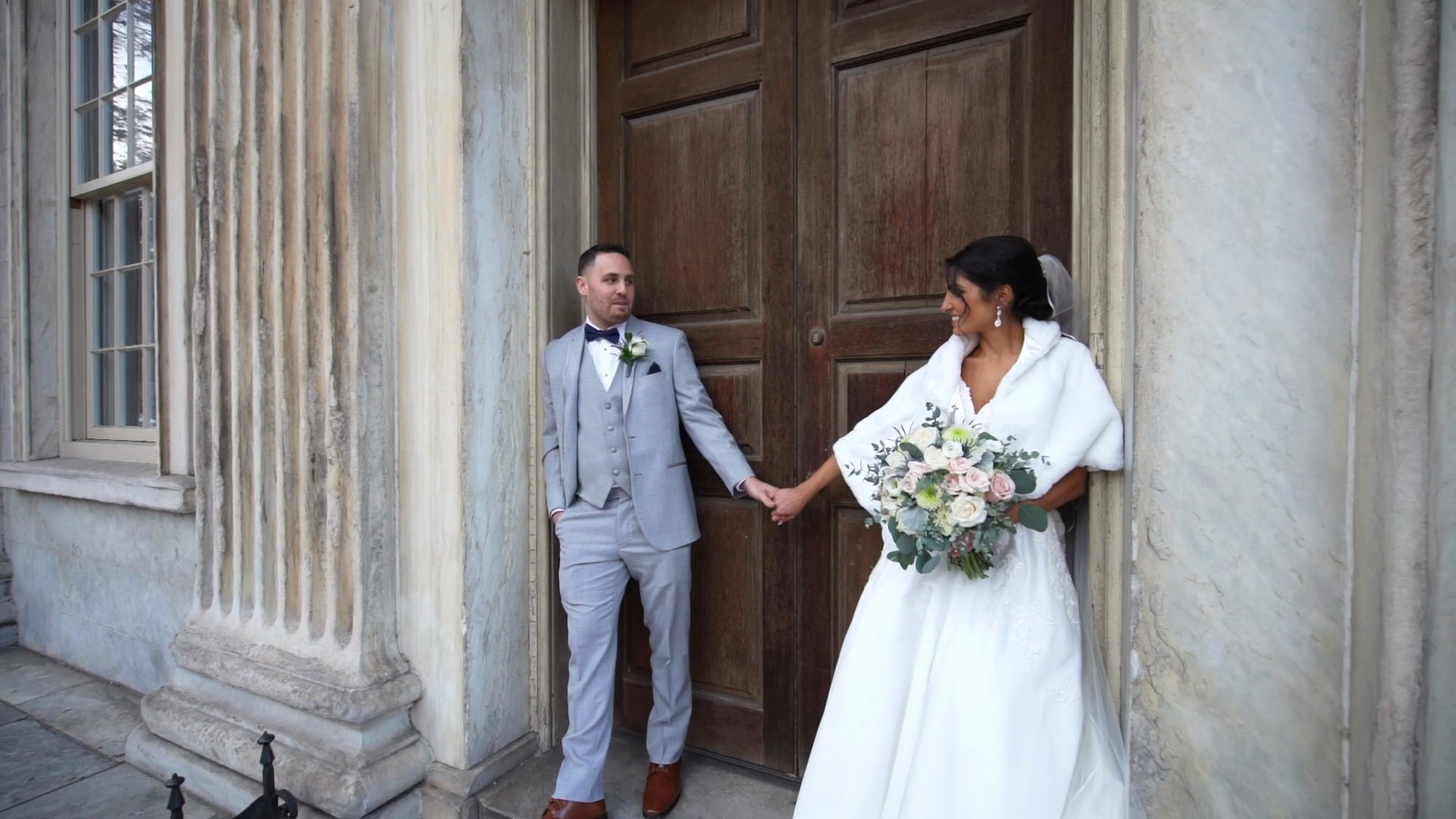 Alyssa and Will holding hands before tall wooden doors between stone columns